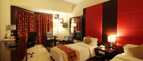 Une chambre d’hôtel avec deux lits, un bureau, une chaise et une table de chevet avec une lampe.