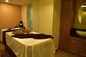 A room with a massage table, a small table with towels and a clock, and a sink with a mirror. - THE SOUTH PARK (Thiruvananthapuram)