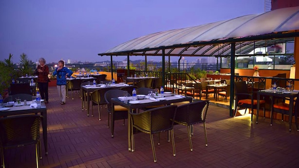An outdoor dining area with tables and chairs, a covered section, and a view of the cityscape. - THE SOUTH PARK (Thiruvananthapuram)