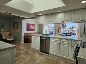 A kitchen with white cabinets, a dishwasher, and a view of a marina through the window.