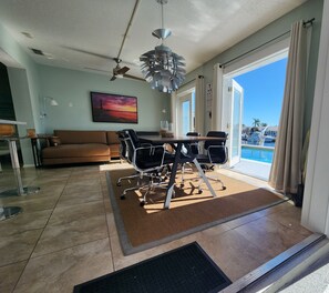 A modern living room with a dining area, a ceiling fan, a painting, and a view of the pool.