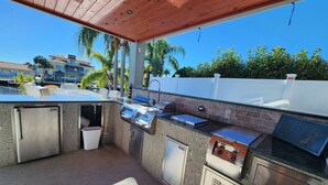 An outdoor kitchen area with a grill, sink, and storage cabinets. - Outdoor lovers dream home- Pool, outdoor kitchen, private dock, and so much more (New Port Richey)