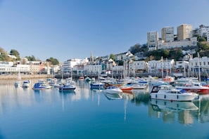 Un port de plaisance avec des bateaux amarrés, des bâtiments en arrière-plan et un ciel dégagé.