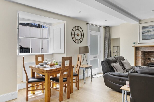 A dining area with a wooden table and chairs, a clock on the wall, and a sofa in the background.