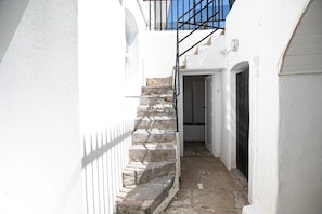 Un escalier étroit en pierre mène à une porte, qui est elle-même entourée de murs blancs et d’une rambarde en métal.
