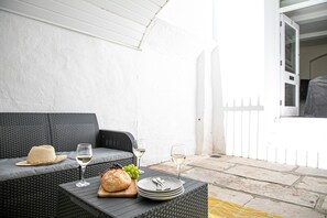 A wicker sofa with a woven hat and two glasses of white wine on a table, a loaf of bread, and a plate with cutlery.