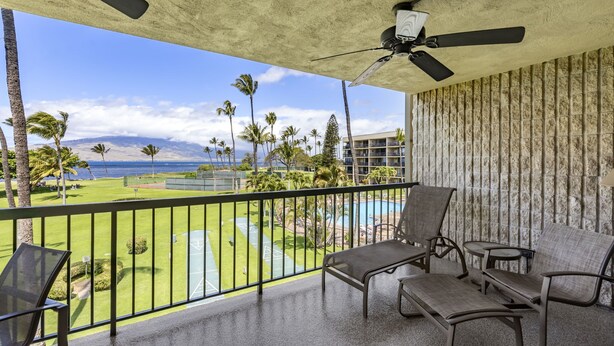 Un balcon avec vue sur un terrain de golf et l’océan, équipé d’un ventilateur de plafond et de sièges.
