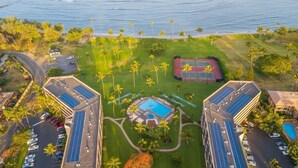 Vue aérienne d’un complexe hôtelier doté d’une piscine centrale, de panneaux solaires et d’un court de tennis.