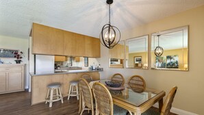 Une cuisine moderne avec des meubles en bois, une table à manger en verre, des chaises en osier et un luminaire suspendu.