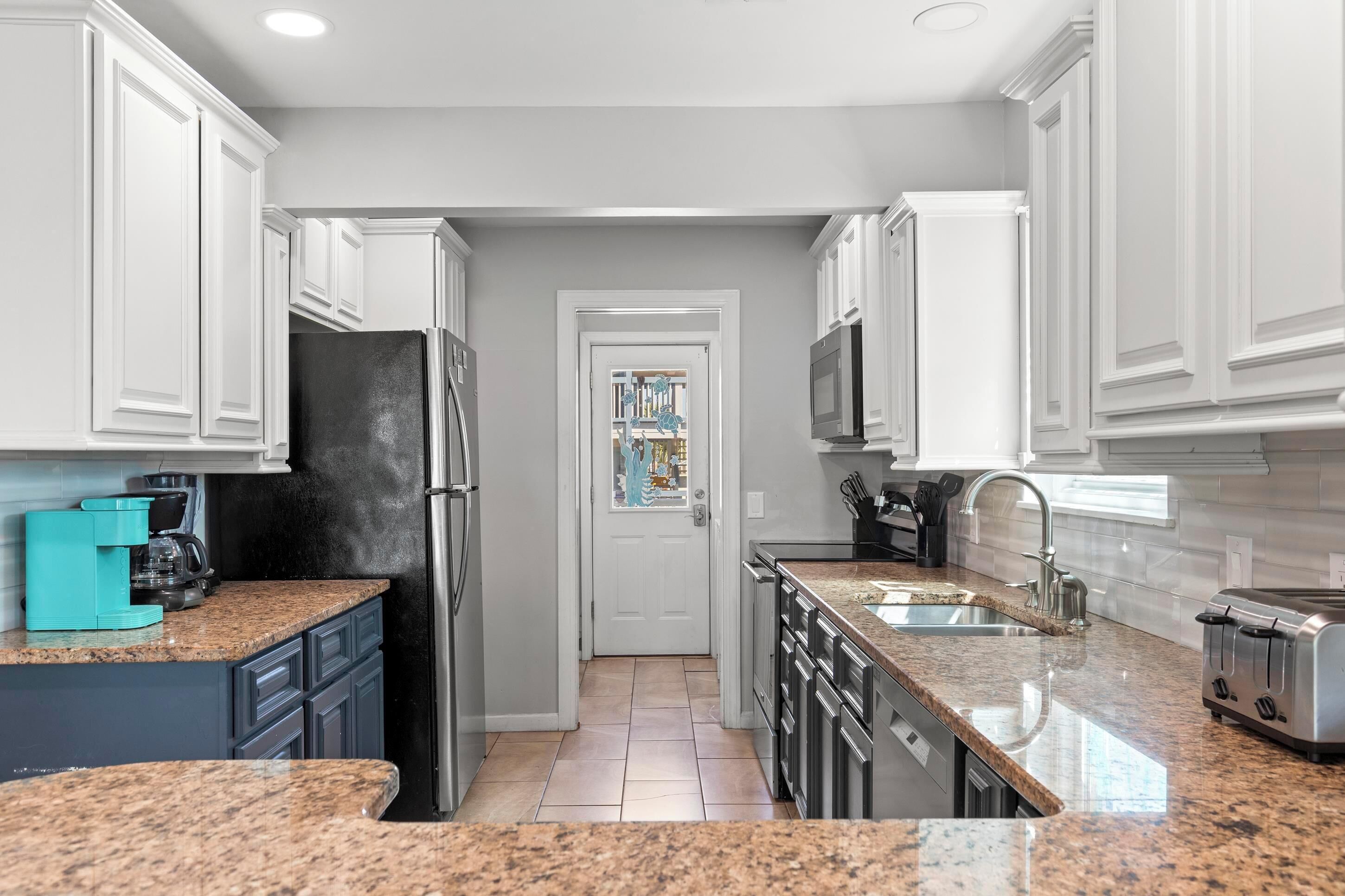 A kitchen with white cabinets, granite countertops, a refrigerator, a toaster, and a sink.