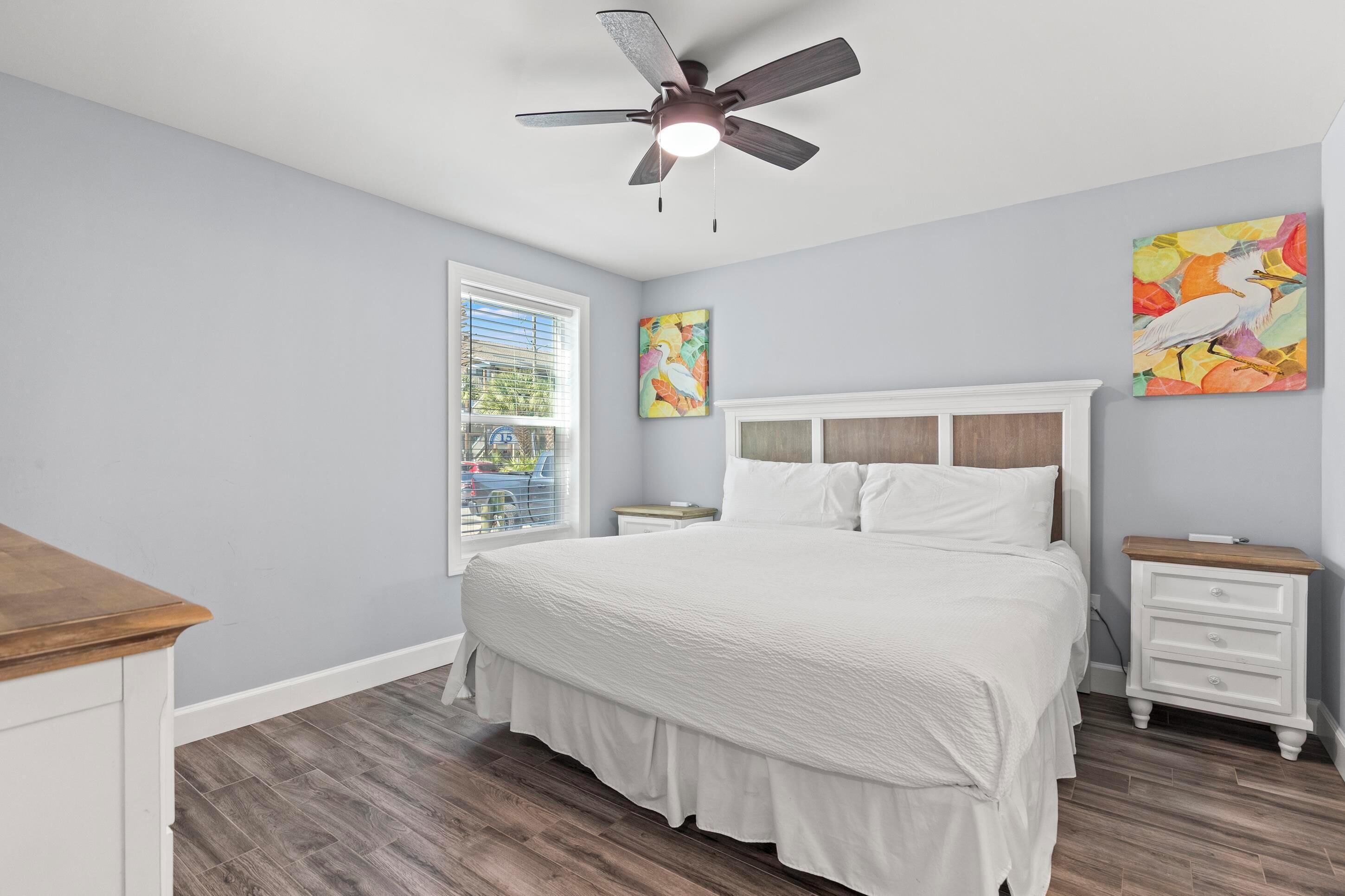 A bedroom with a bed, a nightstand, a ceiling fan, and a window.