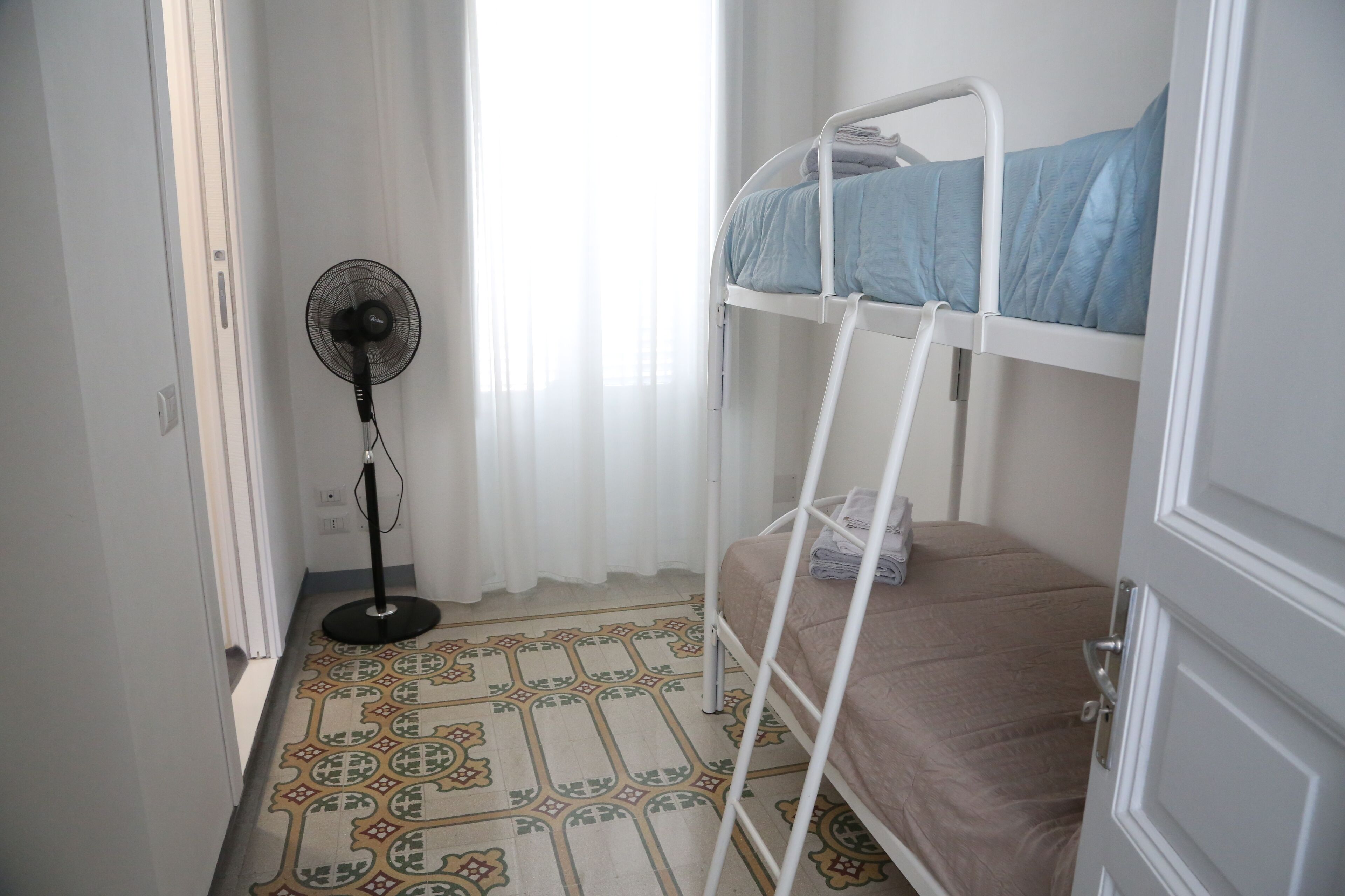 A room with a bunk bed, a standing fan, and a patterned floor.