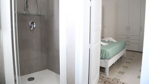 A bathroom with a shower, a toilet, and a bed with a green bedspread. - Palazzo Leonardo 1 (Scicli)