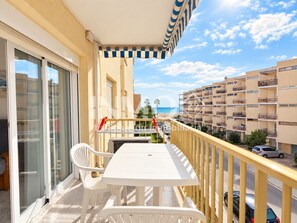 Un balcon avec une table et des chaises, donnant sur une plage et une rangée d’immeubles.