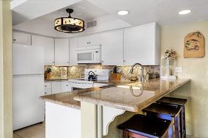 A kitchen with white cabinets, a microwave, a stove, and a sink.
