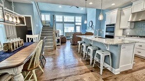 A kitchen with a central island, bar stools, a dining table with chairs, and a staircase leading to another level.