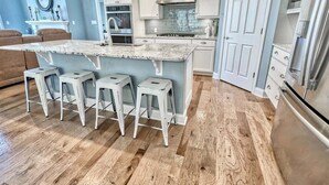 A kitchen with a central island, bar stools, white cabinets, a stainless steel range hood, and a refrigerator.