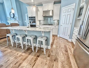 A kitchen with a central island, bar stools, white cabinets, a stainless steel range hood, and a refrigerator. - Coastal Club Community * 19079 * w/ Resort-Style Amenities* 6 Br (Lewes)