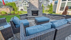 An outdoor patio with wicker furniture, a stone fireplace, and a view of a residential area.