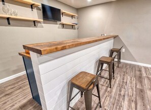 Una zona de bar con mostrador de madera, paneles blancos y dos taburetes.