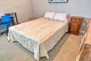 Un dormitorio con una cama, un escritorio, una silla, una mesita de noche y un cuadro colgado en la pared.