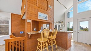 Eine moderne Küche mit Holzelementen, eine Bar mit zwei Hockern und Blick ins Freie.