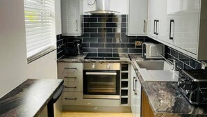 Une cuisine moderne avec des meubles gris, un dosseret en carreaux noirs et des appareils électroménagers en acier inoxydable.