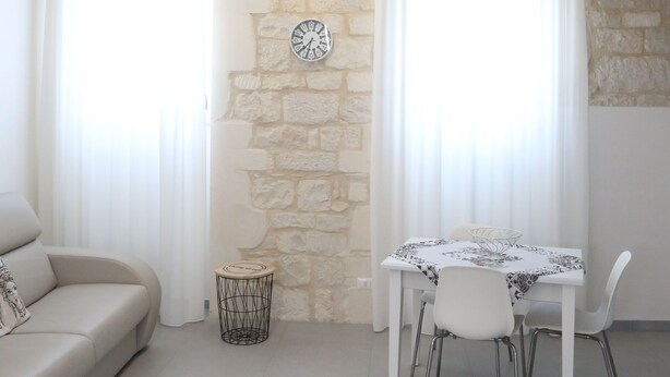 A living room with a stone wall, a sofa, a dining table with chairs, and a small side table.