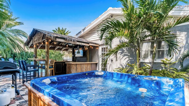 Ein Whirlpool in einem Garten mit einer Pergola, Stühlen und einem Billardtisch.