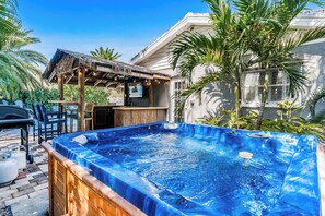 A hot tub in a backyard with a pergola, chairs, and a pool table.