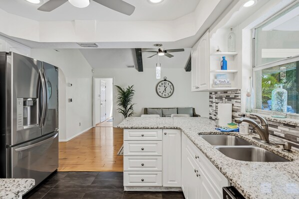 A modern kitchen with white cabinetry, granite countertops, a stainless steel refrigerator, and a built-in oven.