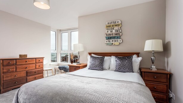 A bedroom with a large bed, wooden dresser, bedside tables, a window, and a wall decoration.