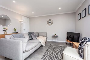 A living room with a grey sofa, a patterned rug, a television, and a wall clock.