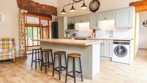 Una cocina moderna con una isla central, taburetes de bar, lavadora y una pared de piedra rústica.