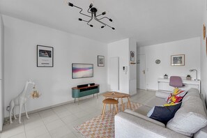 Een moderne woonkamer met een bank, een televisie, een eettafeltje en een decoratieve girafbeeld.