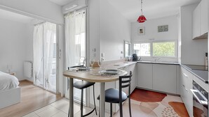 Eine moderne Küche mit Essbereich, weißen Schränken, einer roten Pendelleuchte und einem großen Fenster.
