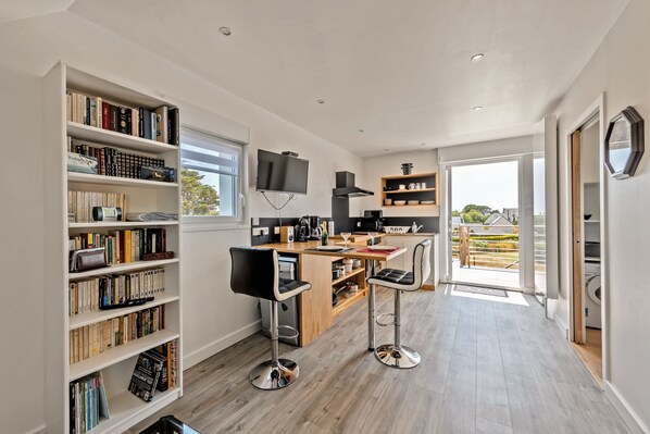 A modern kitchen with a wooden island, bar stools, and a bookshelf filled with books.