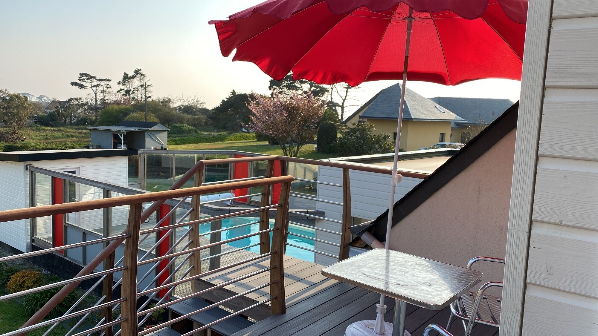 Une terrasse avec une piscine, un parasol rouge et une table.