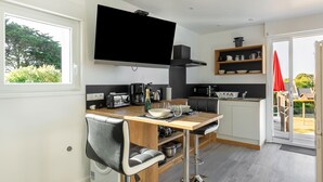 Ett modernt kök med en platt-TV, trästolar till bardisken och ett matbord.