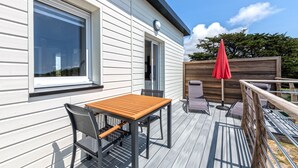 En terrass med ett bord och stolar, ett rött parasoll och ett trästaket.