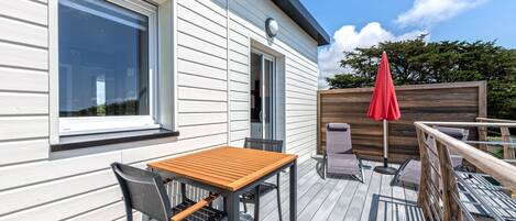 A deck with a table and chairs, a red umbrella, and a wooden fence.