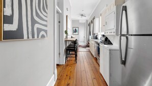 A narrow kitchen with wooden flooring, stainless steel appliances, and a ceiling fan.