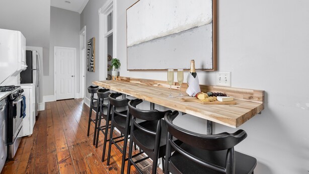 A kitchen with a wooden bar counter, black bar stools, a white refrigerator, and a large abstract painting on the wall.
