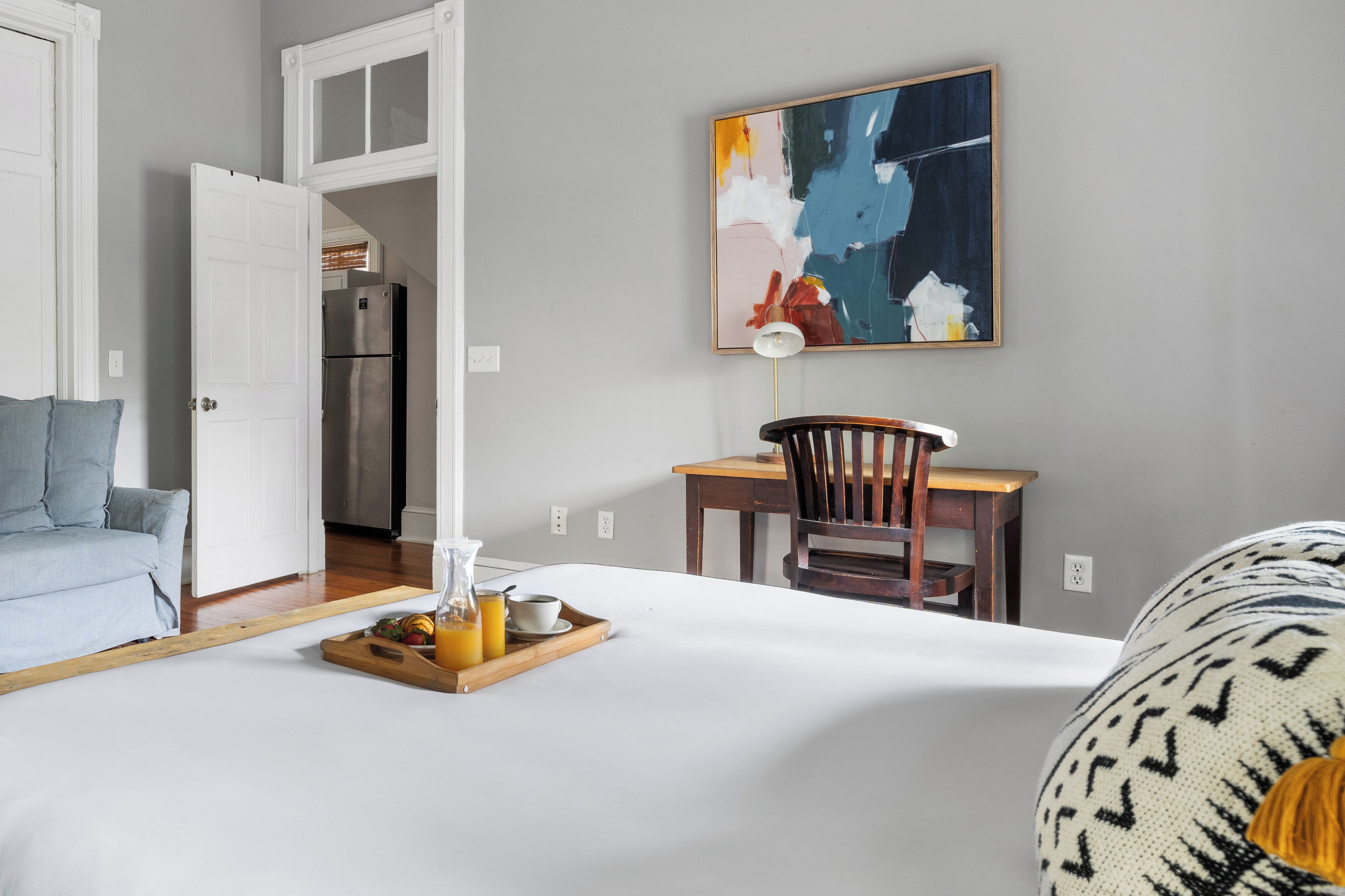 A hotel room with a bed, a dining table with a chair, a refrigerator, and a painting on the wall.