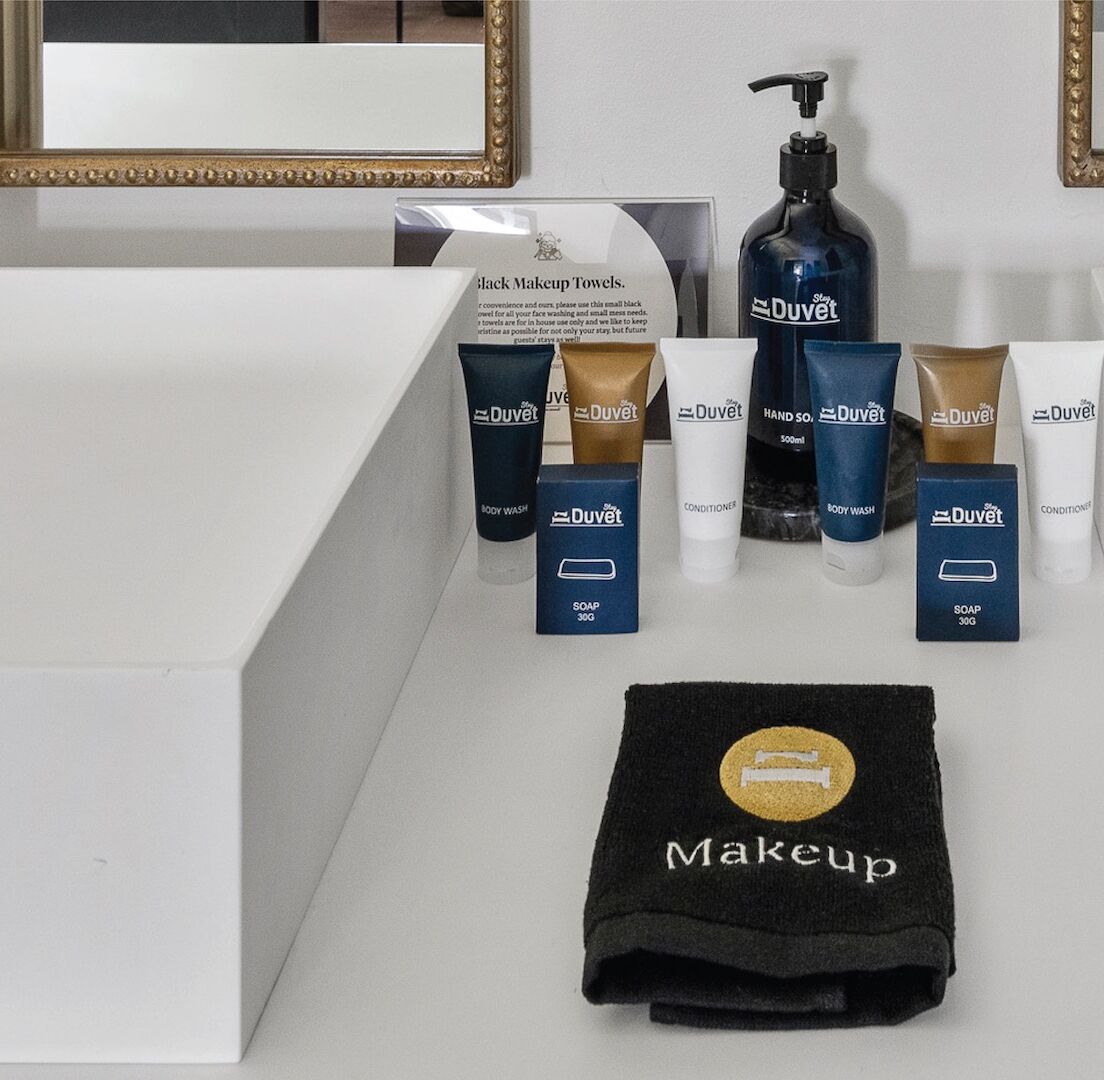 Un mobile bagno con un asciugamano nero per il trucco, diversi prodotti per la cura personale DuVet e uno specchio con cornice dorata.