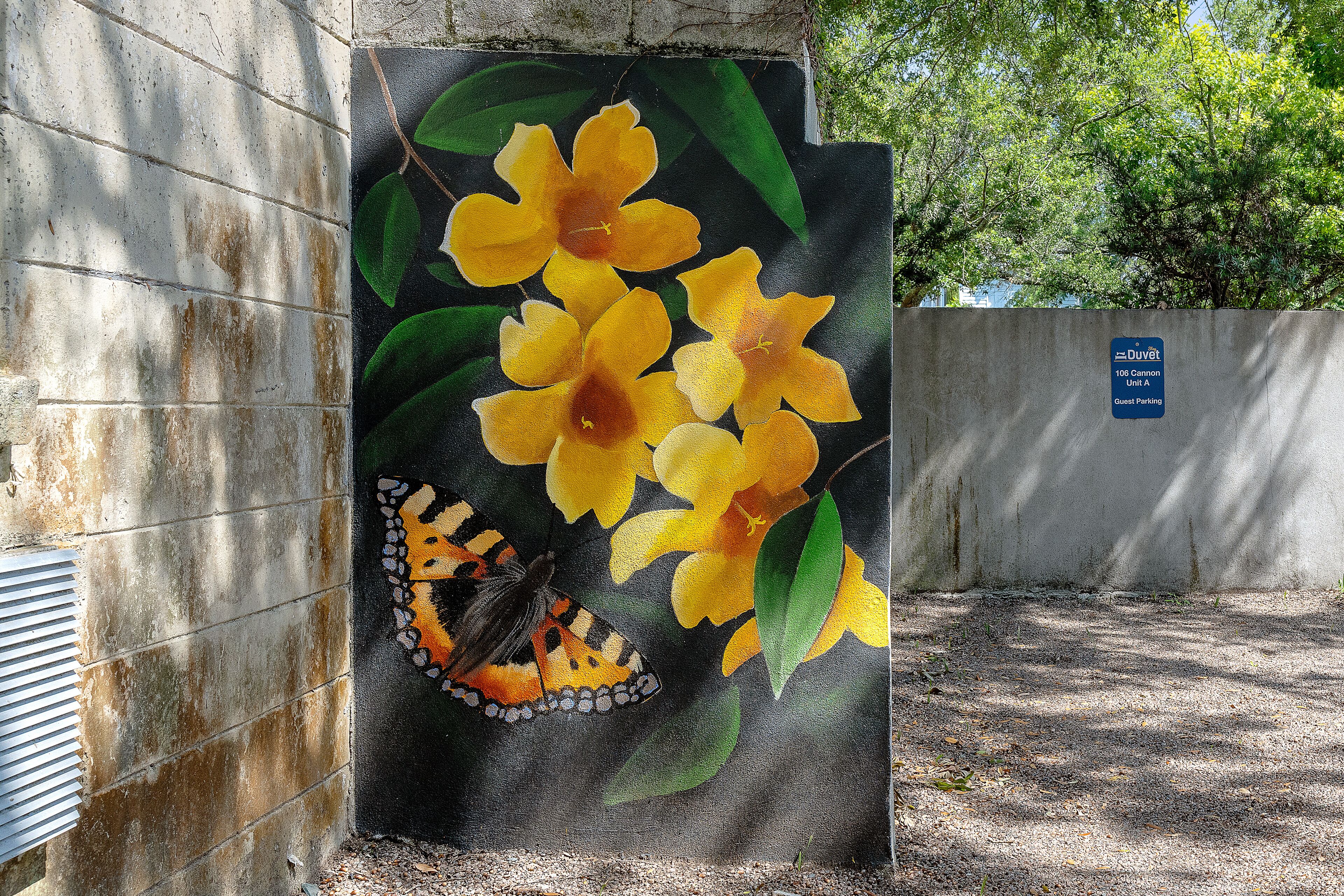 A concrete wall with a mural of yellow flowers and a butterfly. A sign indicates it's a guest parking area.
