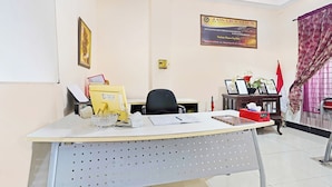 A reception desk with a computer, a chair, a small table with a vase of flowers, and a framed certificate on the wall. - OYO 91322 Jawara Guest House Syariah (Bandung)