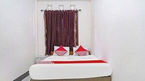 A neatly made bed with white bedding and red accents, a wooden headboard, and a window with patterned curtains. - OYO 91322 Jawara Guest House Syariah (Bandung)