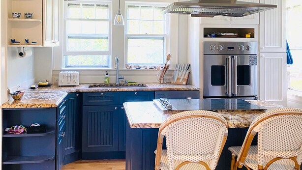 Een keuken met donkerblauwe kastjes, een rvs afzuigkap, een inbouwoven en een groot kookeiland met barstoelen.