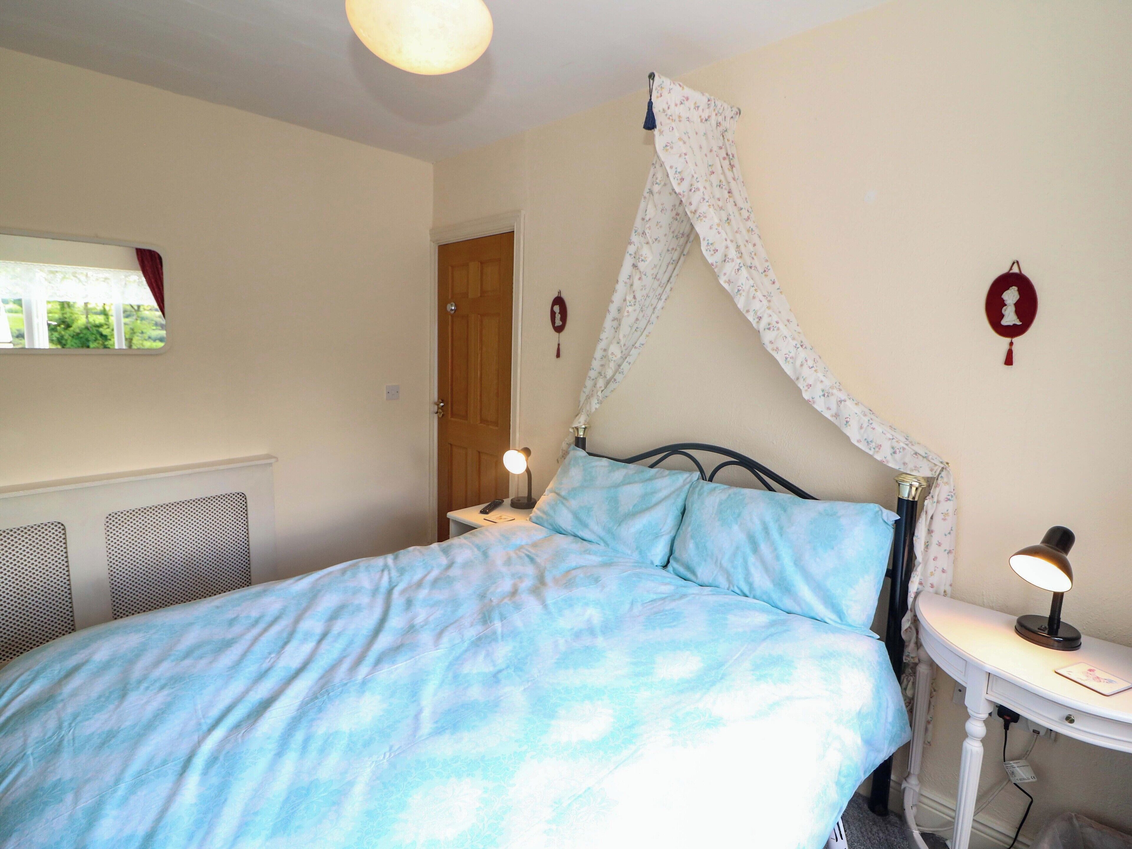 A bedroom with a bed, a nightstand, a lamp, and a window with curtains.